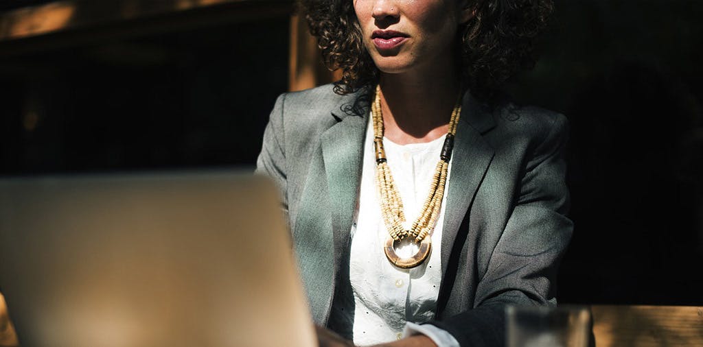 Torso of woman in a blazer sitting at a desk with a laptop