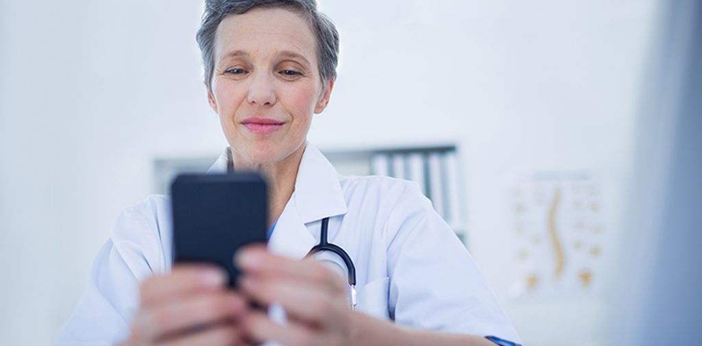 A middle aged female doctor in a doctor's office looking at a phone