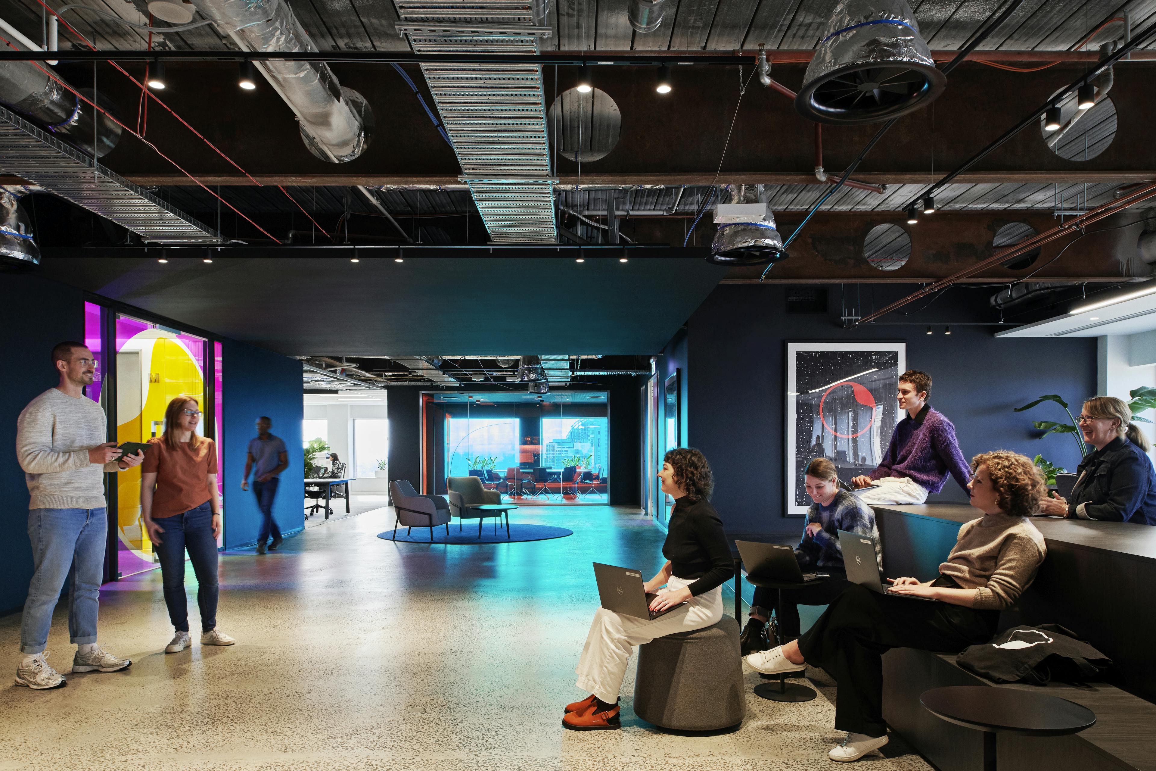 Open work space with 2 people standing in front of a small group presenting.