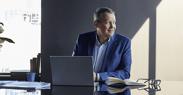 Middle aged white man in a suit sitting at a desk with a laptop